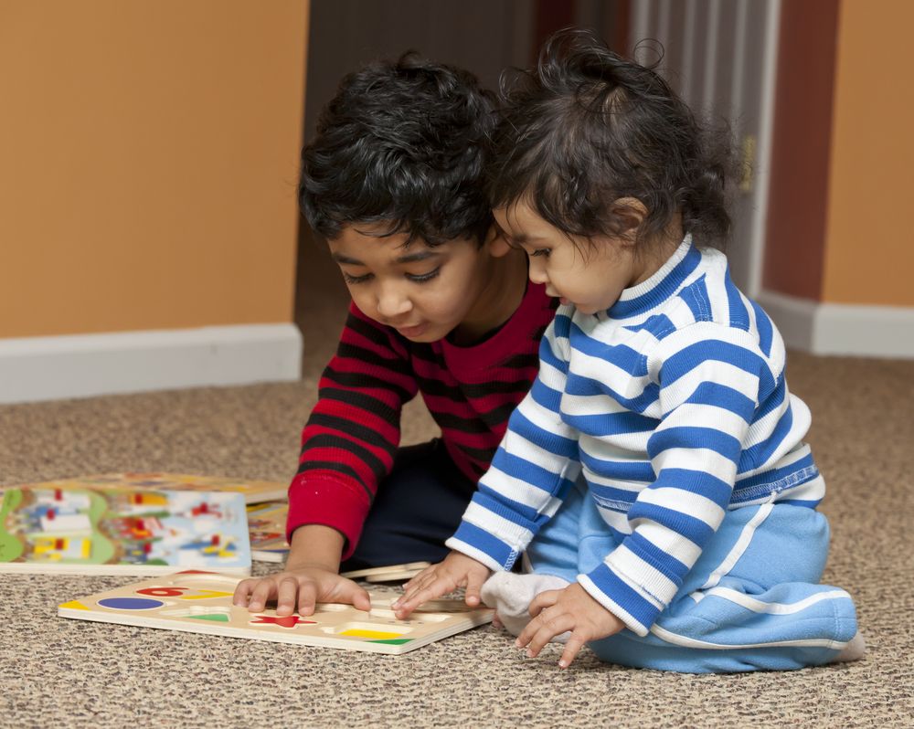 A brother and a sister play with puzzles pieces.