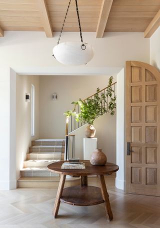 White entryway with light wood panelled ceiling, parquet floor and round central wooden accent table