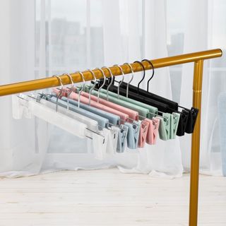 Various colors of non slip hanger with plastic clips on a gold rail against a background of net voile floor length curtains