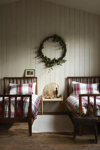 A shared bedroom with two single beds made with check/tartan bedding sets, Christmas wreath in between beds, shiplap wall decor and cream rectangular rug