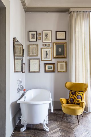 Free-standing bath and yellow chair on parquet flooring with multiple framed pictures above