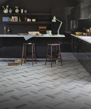 A dark kitchen scheme with an example of multi-toned, wood-effect vinyl kitchen flooring ideas laid in a herringbone style.