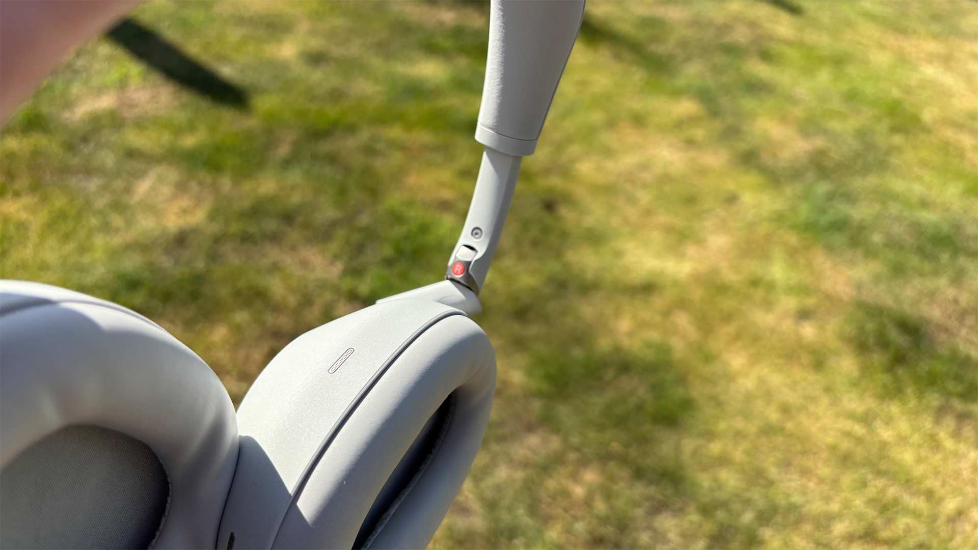 Sony WH-1000XM6 over-ear headphones held above lawn showing detail of earcups