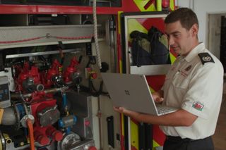 A Welsh firefighter working on a Microsoft laptop while standing