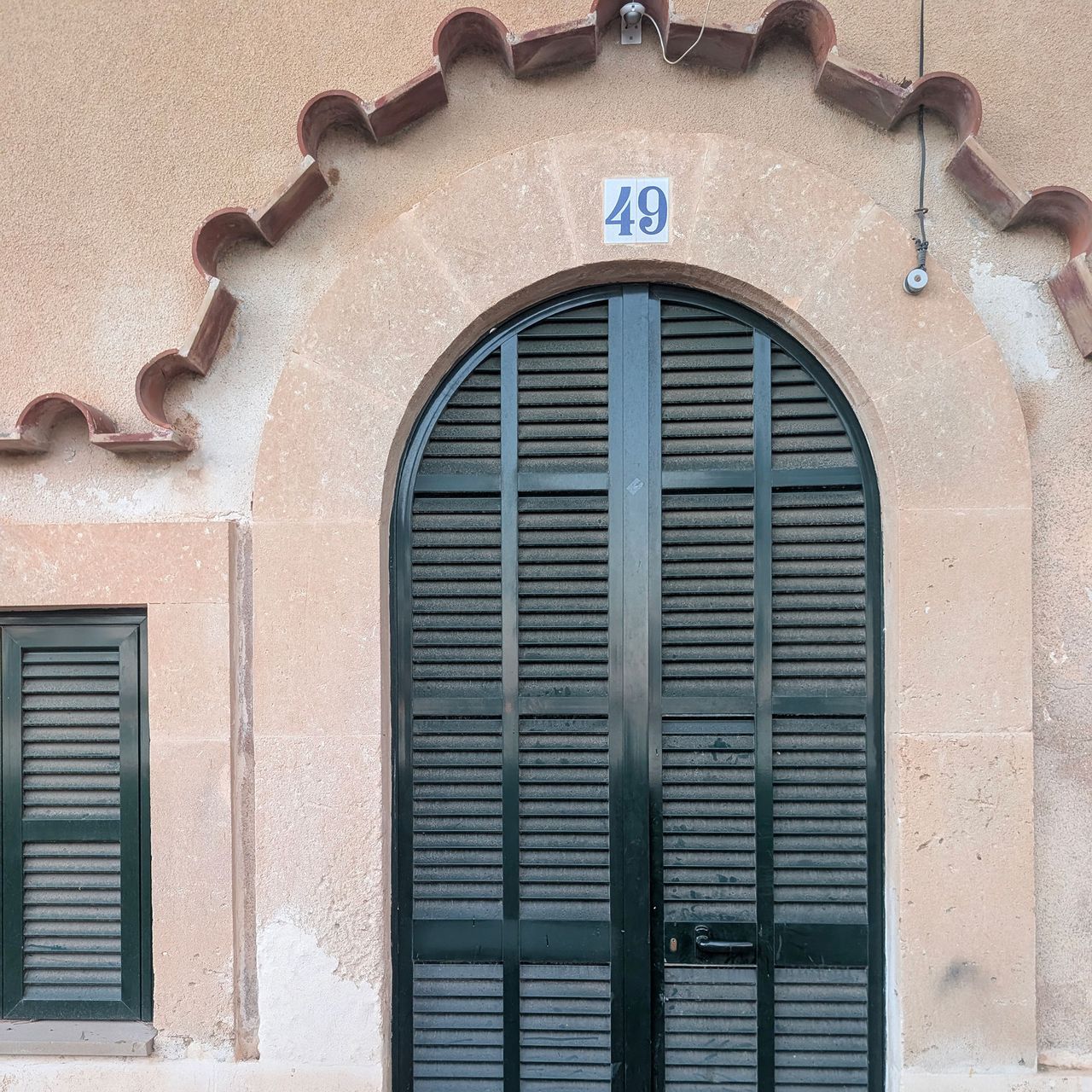 Orange stone building with arched door with dark green/black shutters