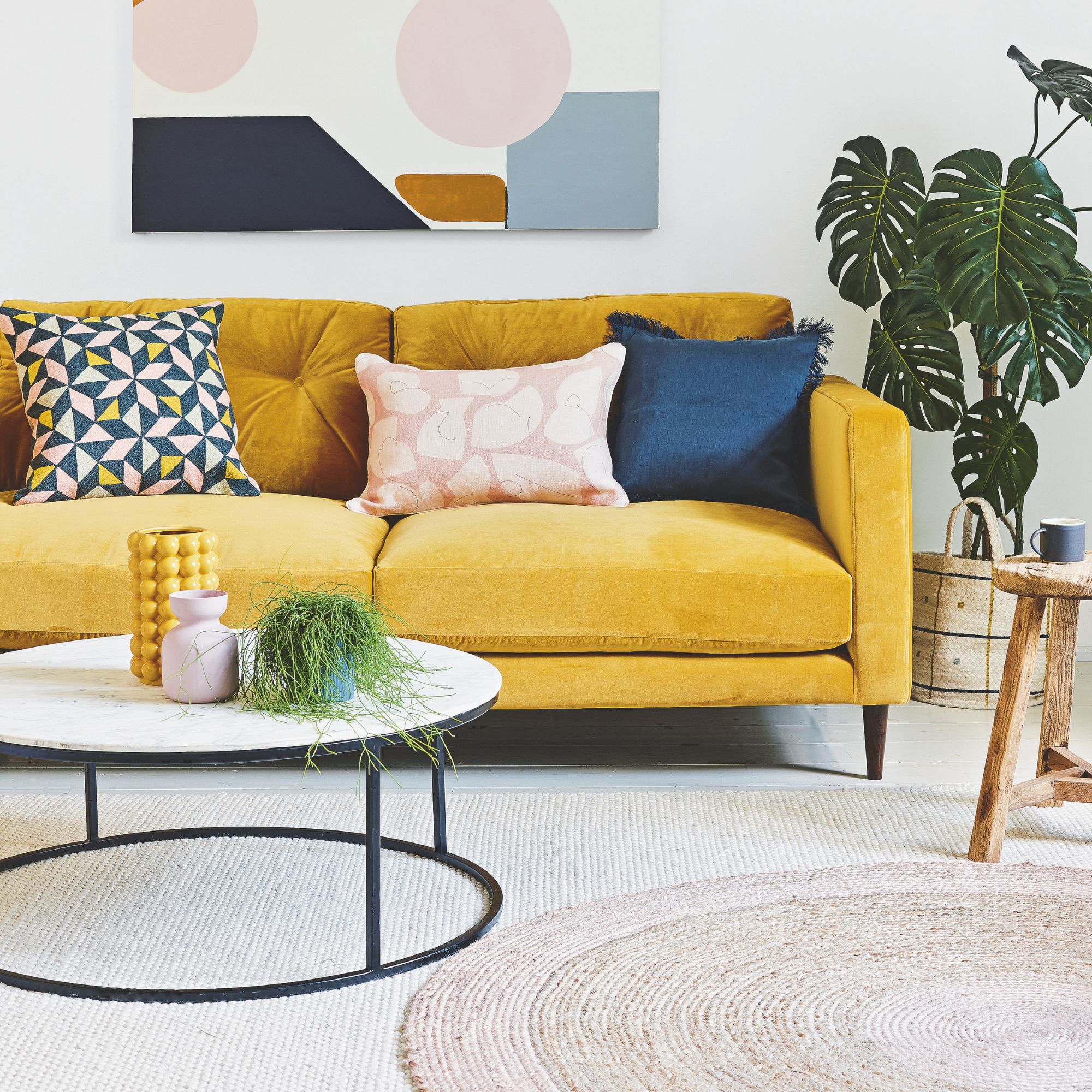 White living room with a yellow sofa and bright cushions on it, on top of wool rugs