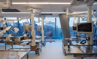Interior view of the new Medical Center for New York’s Columbia University. A room filled with medical equipment. On the far wall, there are panoramic windows that look out to the city.
