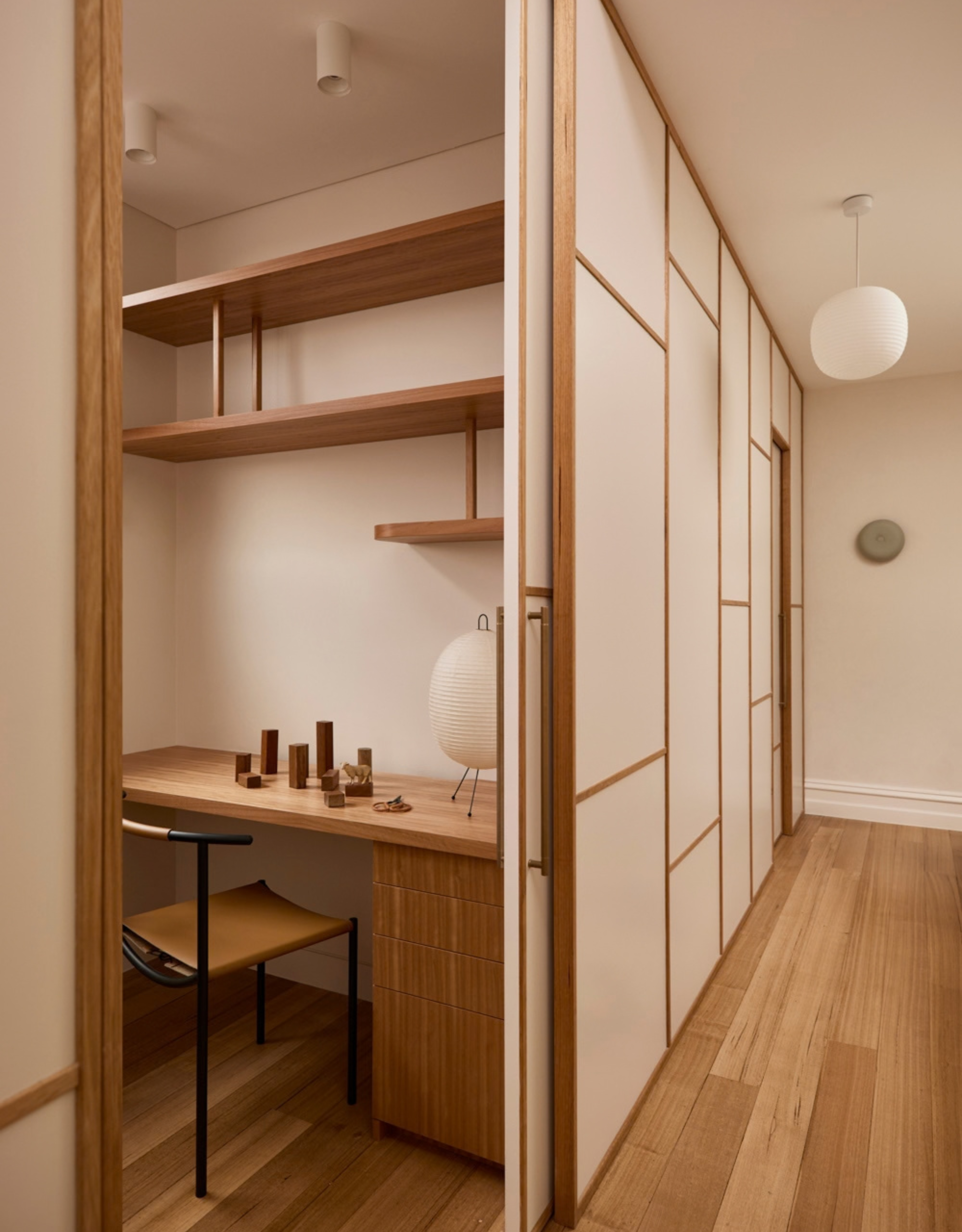 A Japanese home with a small study with a wooden desk, a rice paper table lamp, and sliding doors