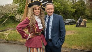 Fiona Dolman in a red jacket and black pirate hat as Sarah Barnaby alongside Neil Dudgeon in a suit as DCI Barnaby in Midsomer Murders
