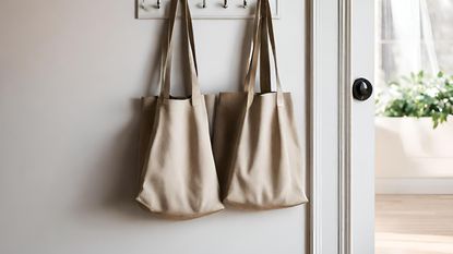 Two tote bags hanging from hooks against a white wall - AI generated image