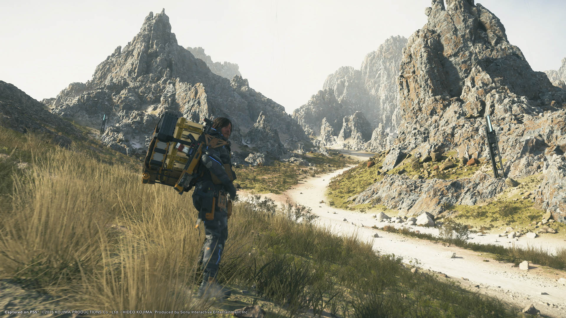 Sam Bridges stands in grass near a dirt road in Death Stranding 2: On The Beach