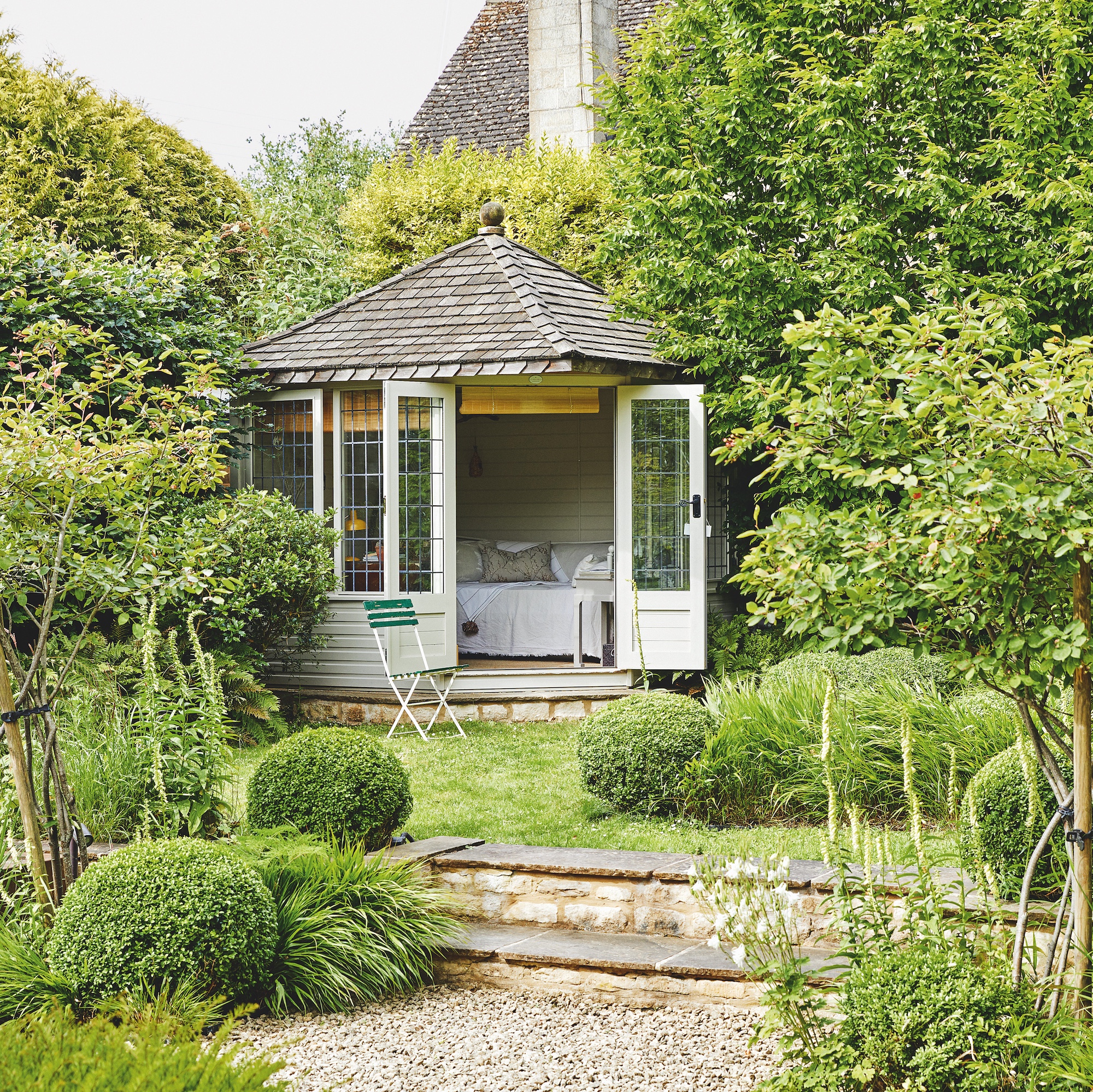 summer house in English garden with box balls, lawn and shrubs, with two steps and gravel area