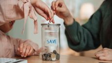 Two hands putting coins in a jar that says "save"