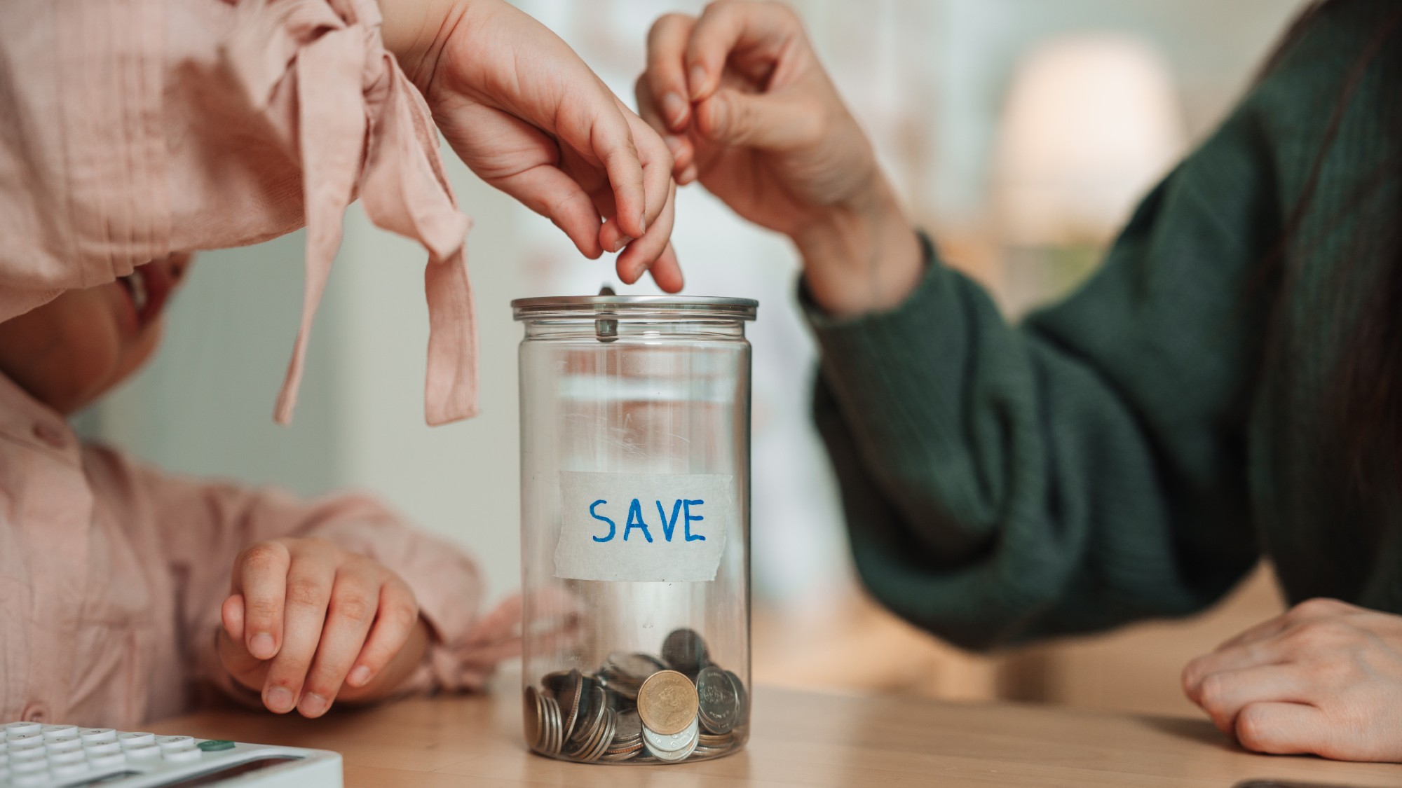 Two hands putting coins in a jar that says "save"
