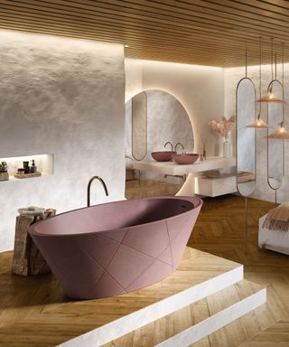 Spa like bathroom design with fluted, wooden paneled ceiling, textured white walls, large rounded mirror, two oval mirrors attached to the floor and ceiling, striking freestanding bath design in a warming taupe, matching sink, bath positioned on a stepped level, three hanging shades in a cluster, wooden accessories.