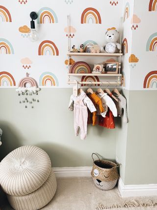 A children's bedroom or nursery with rainbow wallpaper and a shaker peg shelf with children's clothes hanging from it