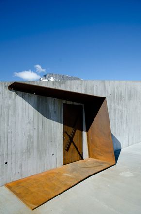 View of a rusted steel door and shelter at the Trollstigen Visitor Centre under a blue cloudy sky