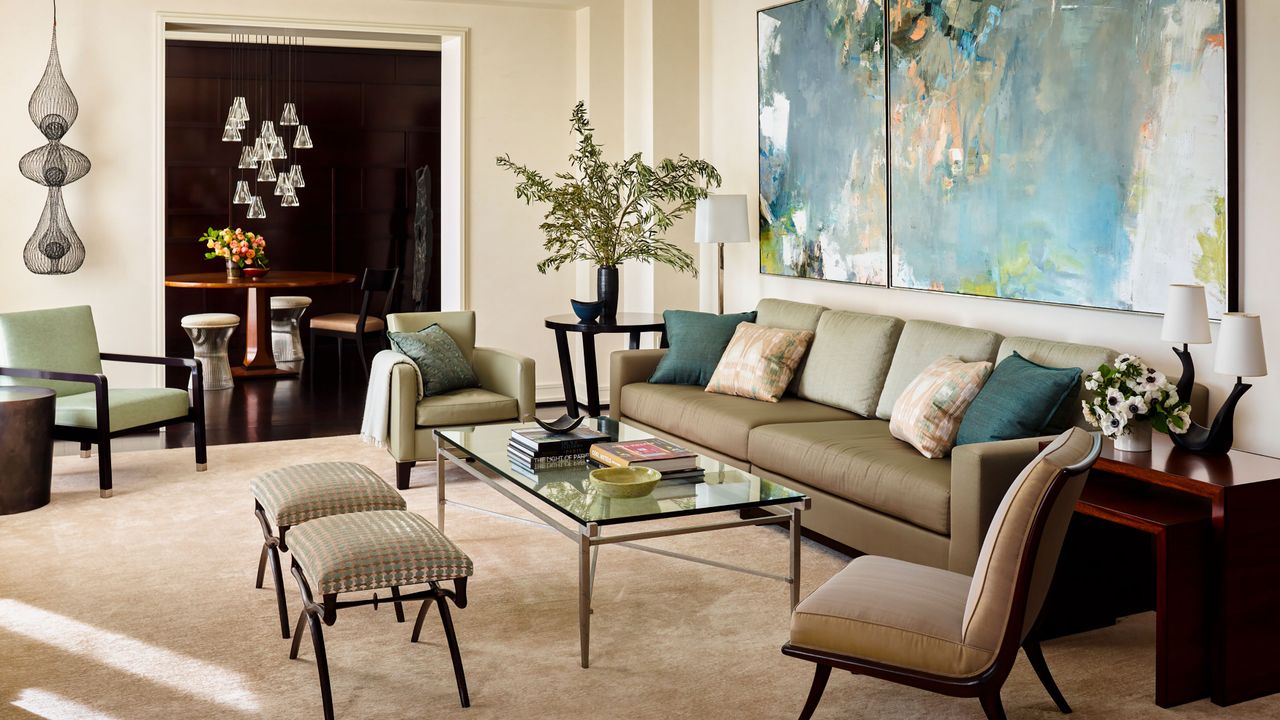 living room with neutral walls and big artwork with taupe sofas and glass coffee table view to dining room