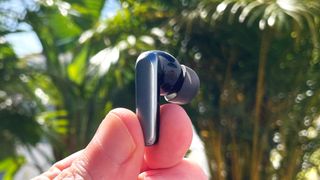 EarFun Air 2 showing left earbud held between fingertips with green foliage in background