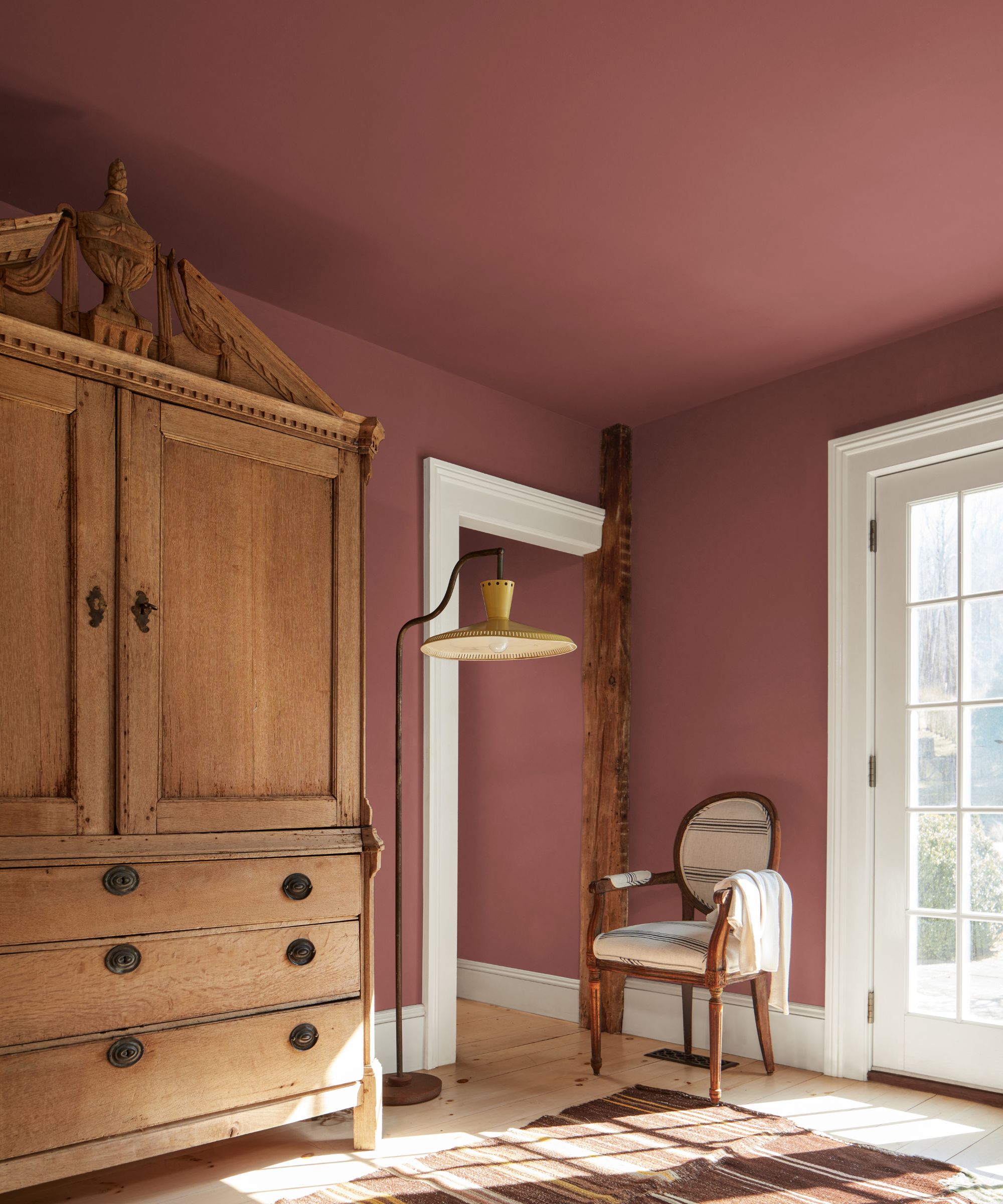 Bedroom painted in Southwest Pottery by Benjamin Moore, a vintage armoire, a yellow floor lamp, an antique chair, and a brown striped rug.
