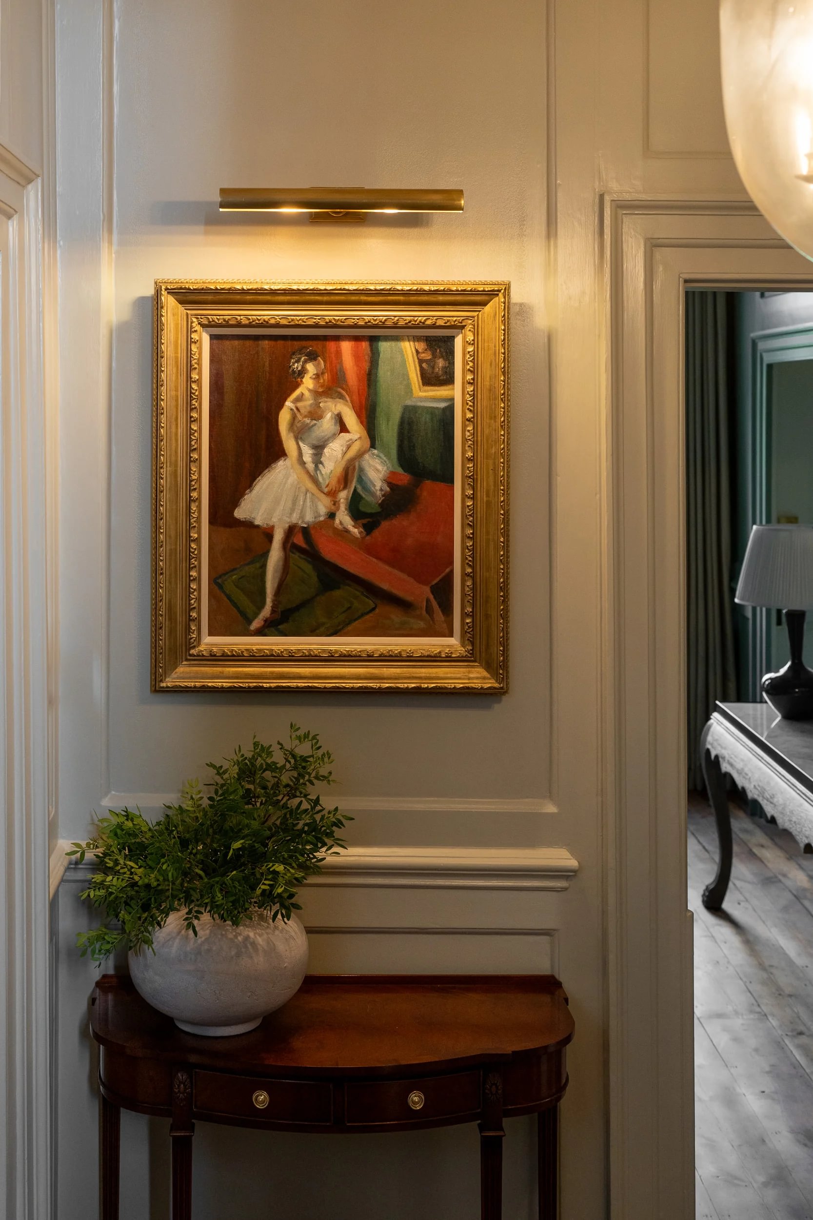 A traditional home with a piece of artwork framed in gold and picture light above