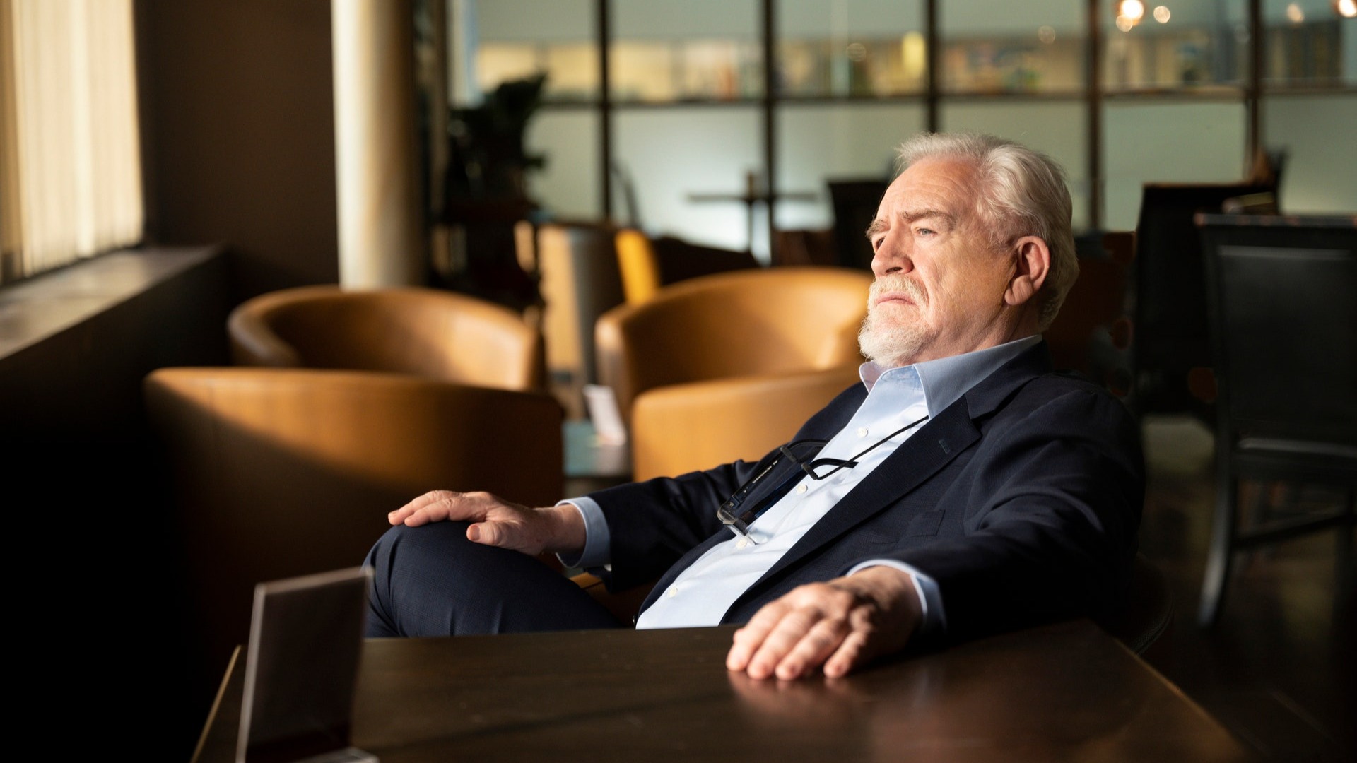 Logan Roy de Brian Cox se sienta en una mesa mirando por la ventana en la temporada 3 de Succession