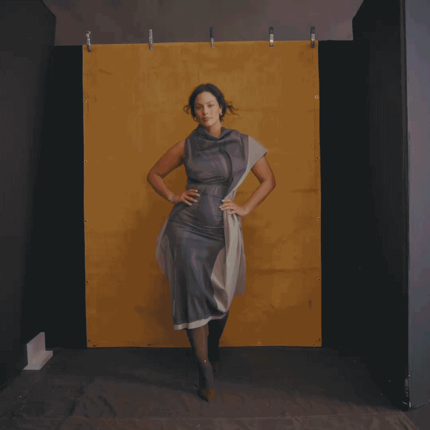 a brunette woman wearing a white and gray dress on a tan background in a moving gif