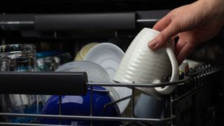 A white mug being removed from the upper basket in a dishwasher