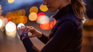 a photo of a woman adjusting her running watch outside at nighttime