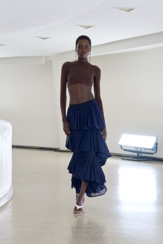 a model wears a brown crop top and a navy blue ruffle skirt