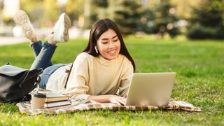 Happy student girl with laptop preparing for exams, sitting on grass
