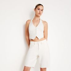 model wears white vest and white long jean short and white heel in front of a white background