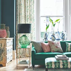 A living room painted in dark teal green with an emerald green sofa