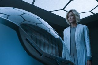 Dr Catherine Halsey (Natascha McElhone) in a private room in her lab, standing in front of an egg-shaped pod. The pod has a glass roof, which is reflecting the hexagonal pattern from the ceiling.