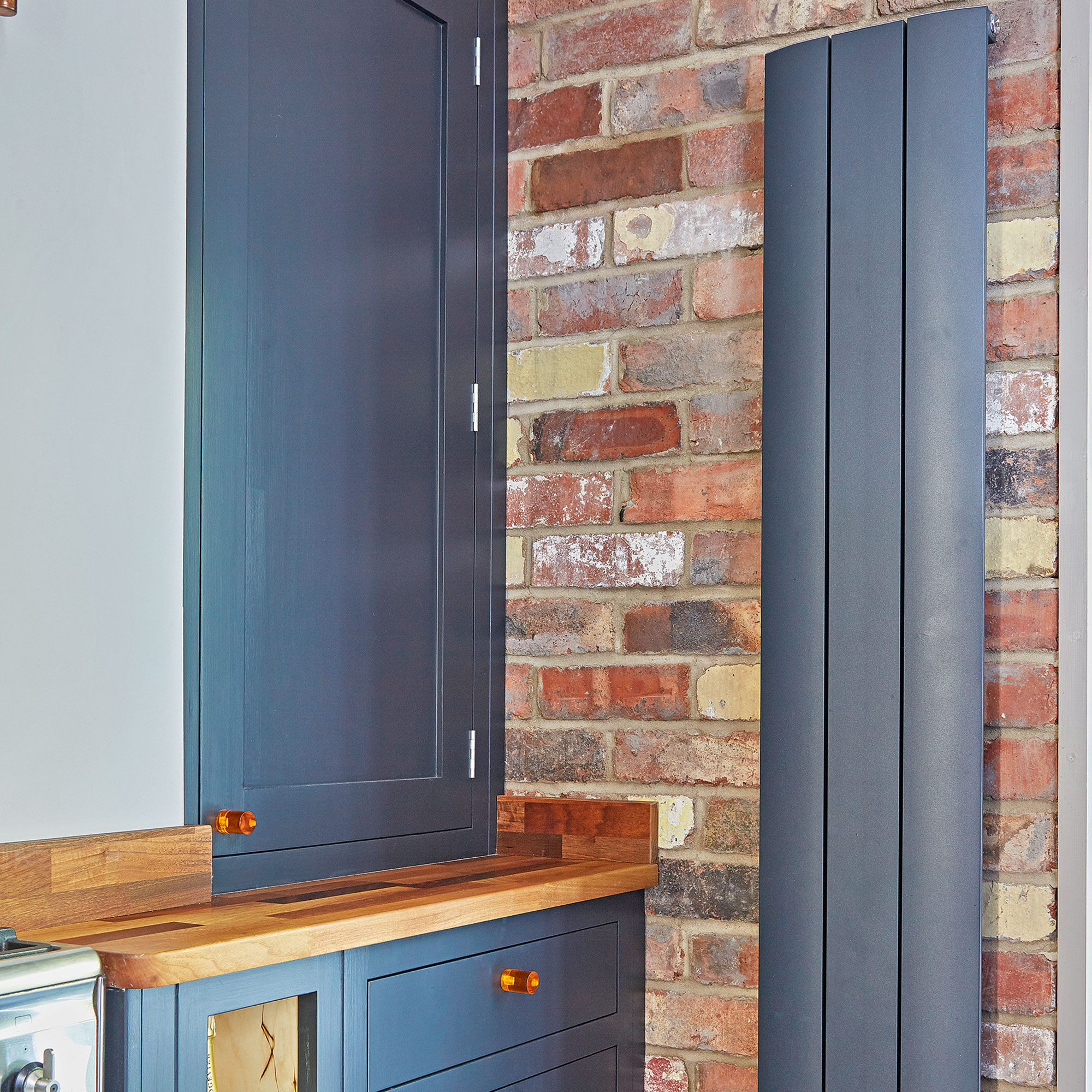 Blue kitchen cabinets next to exposed brick wall and contemporary slim radiator.
