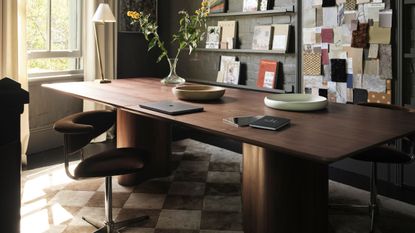 Image of an office with olive green walls and a large wooden desk with brown desk chairs around it. 