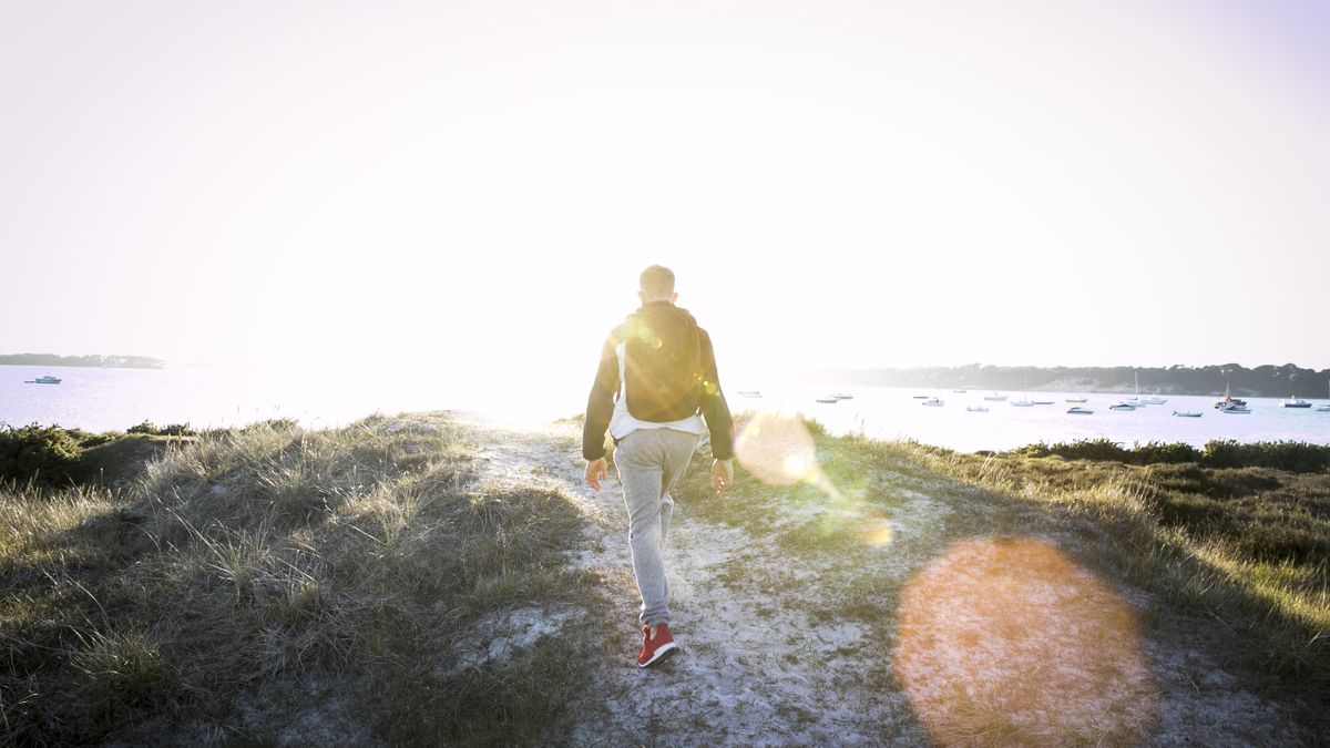 Rear view of young man hiking along sand dunes