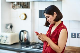 woman wearing red blouse looking at her phone in the kitchen at home