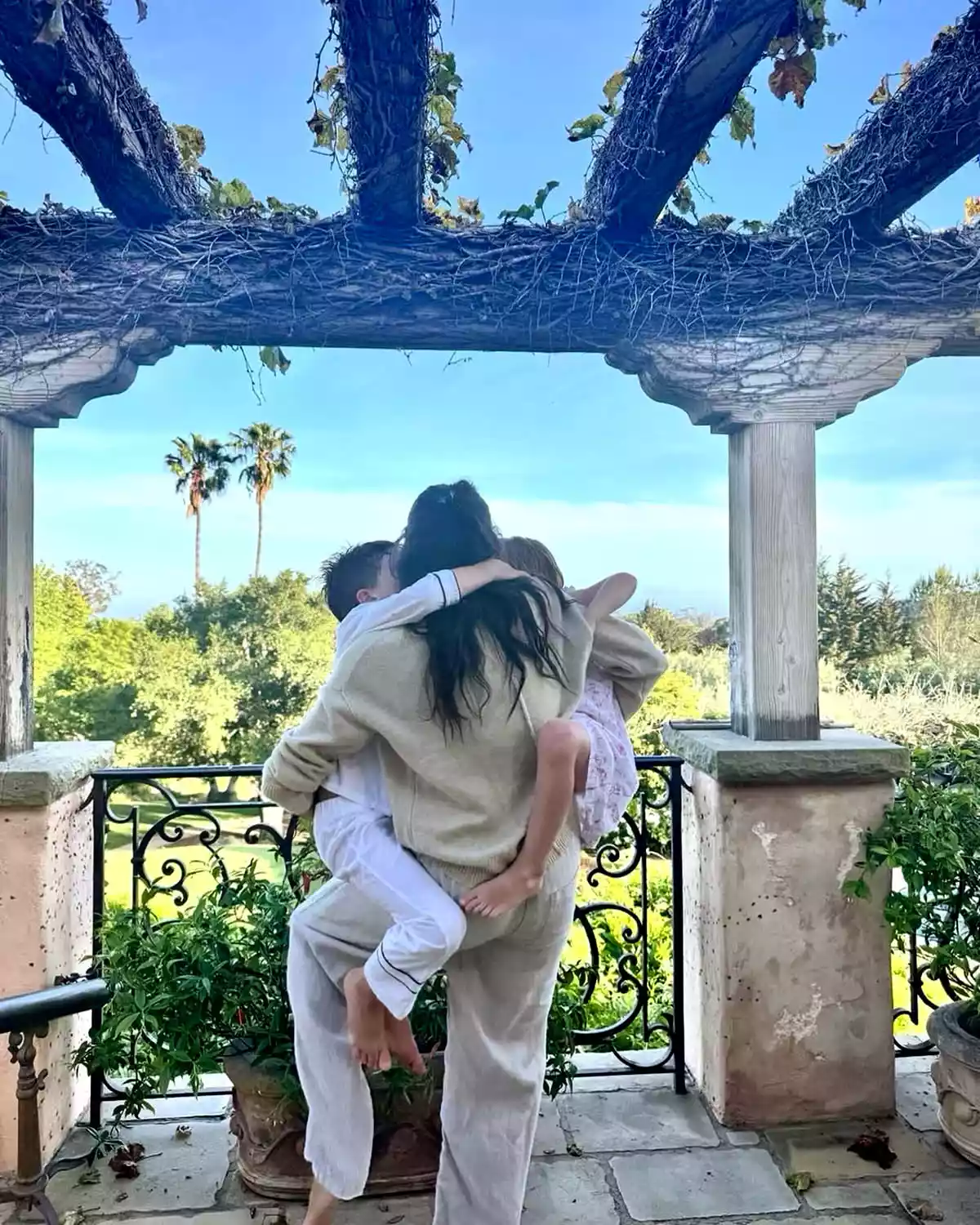 Meghan Markle holding her two kids on a patio with palm trees behind them