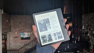 En person som håller upp en Kindle Oasis med ett rum i bakgrunden med tegelväggar.