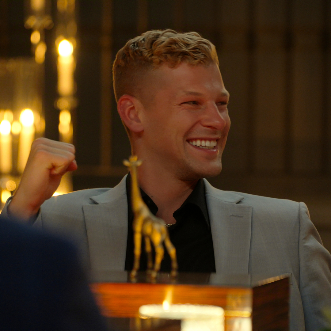 million dollar secrt season 2 winner nick pellechia smiles and holds up his fist at the main table in the stag as the cast looks through their boxes