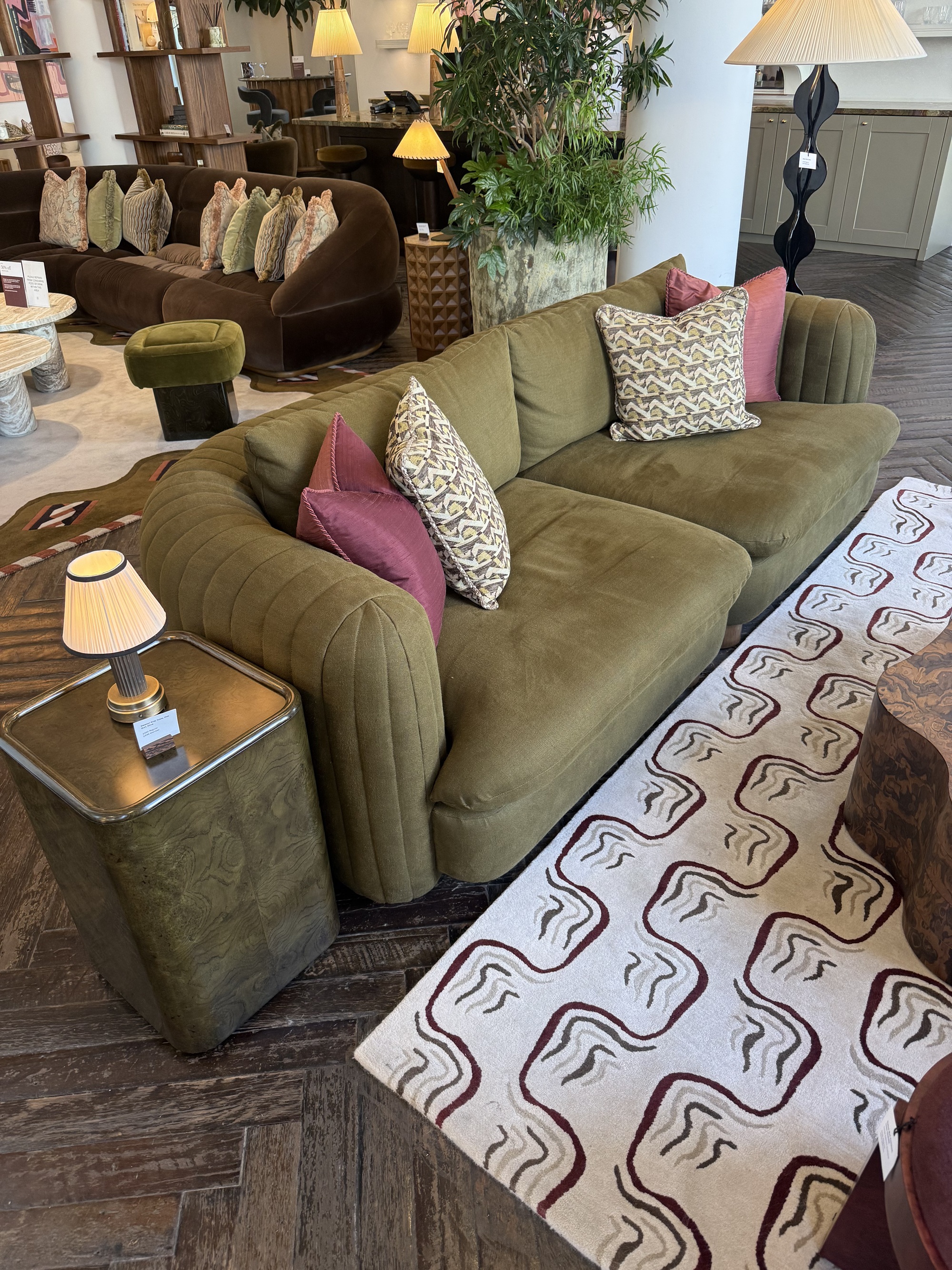 green soho home sofa with cushions on patterned rug with burl side table with lamp, and timber coffee table on dark herringbone flooring