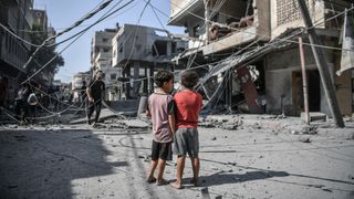 Palestinians are seen by debris of destroyed buildings after Israeli airstrikes hit Khan Yunis, Gaza on October 11, 2023. 