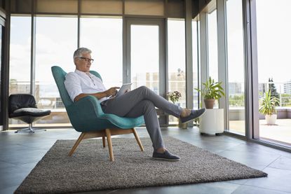 Mature man sitting in armchair at home using tablet