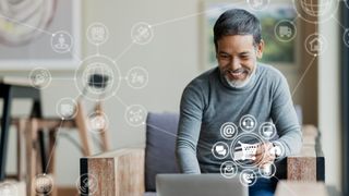 Smiling man looks at laptop with a shopping cart and other symbols floating in the air