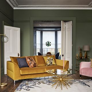 living room with moss green coloured wall and pillows on golden sofa