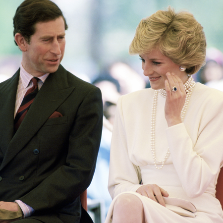 King Charles wears a suit and talks to Princess Diana who looks coy wearing a cream dress, a pearl necklace, and her engagement ring