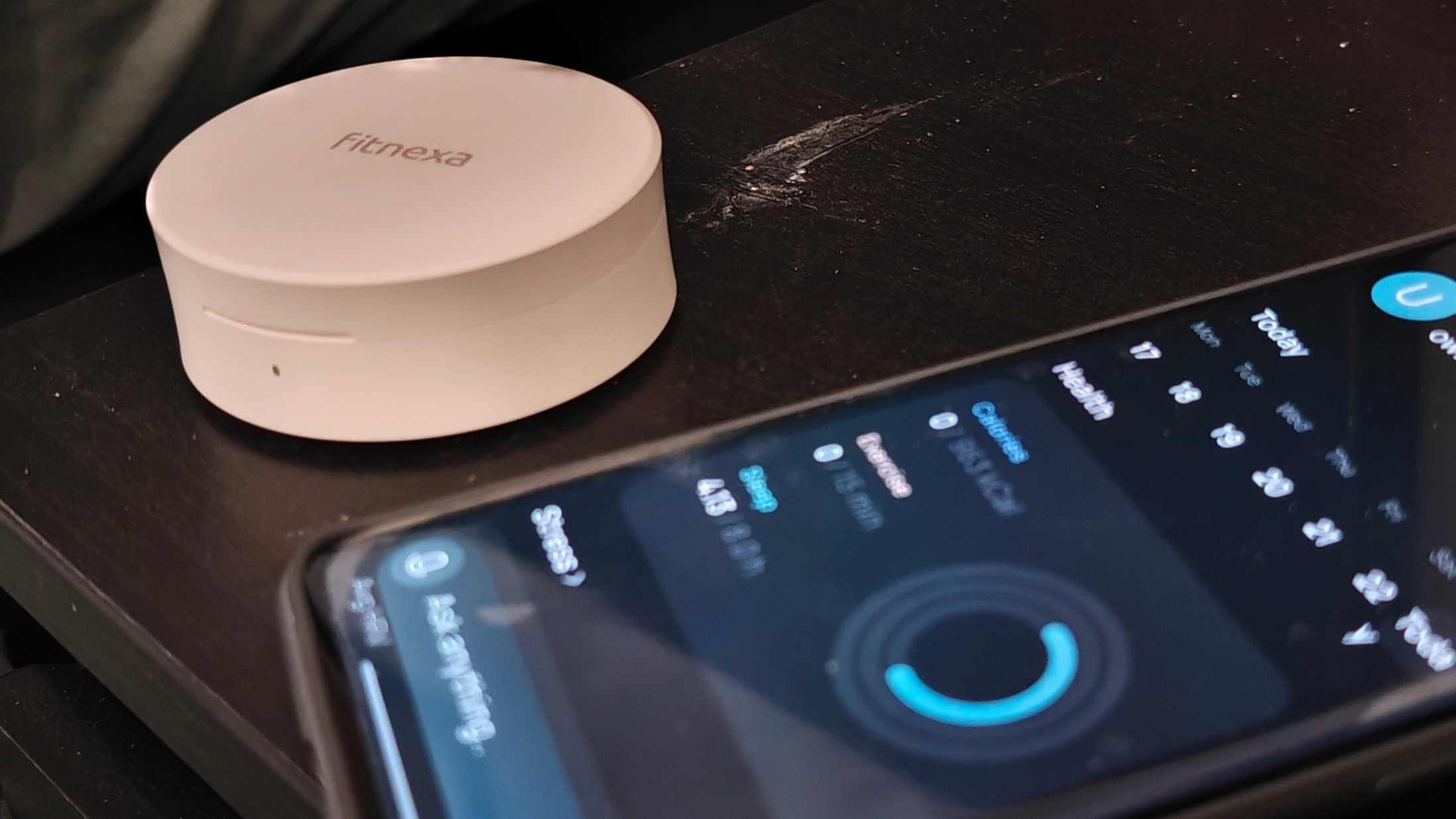 The Fitnexa SomniPods 3 case, closed, next to a smartphone showing the Fitnexa app.