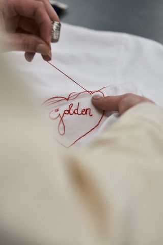 Hand stitching the word ‘Golden’ in a heart on a white shirt