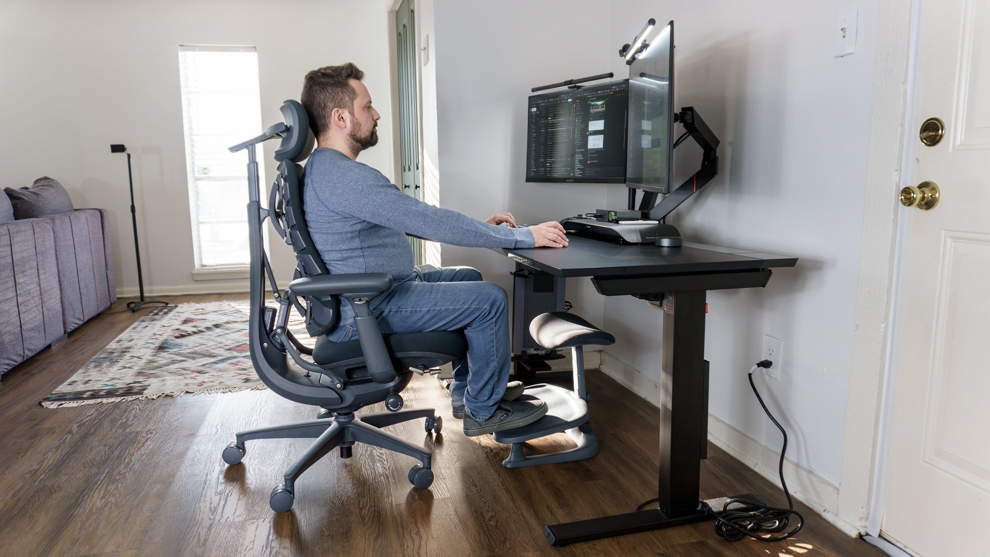 A person sitting on the LiberNovo Omni office chair with their feet up on the LiberNovo StepSync footrest in front of a desk